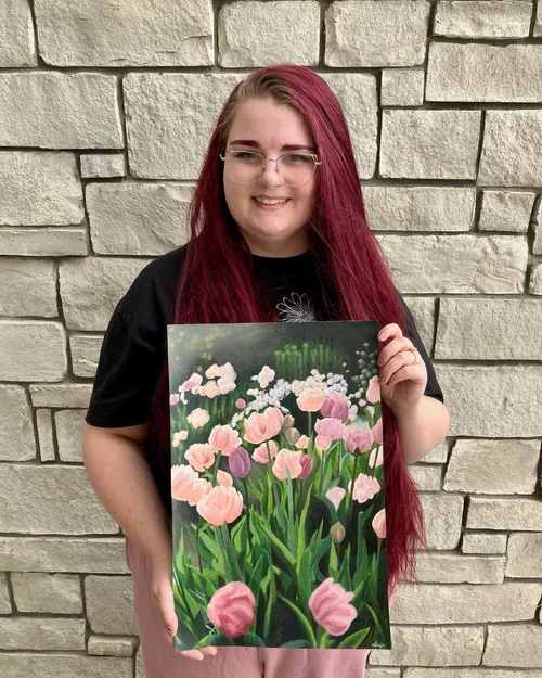 Elise Jackman in front of a brick wall holding a painting of flowers that she created