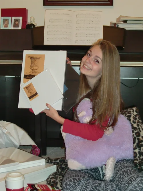 Elise Jackman as a teenager in front of a piano, holding some prints of original an art piece she made