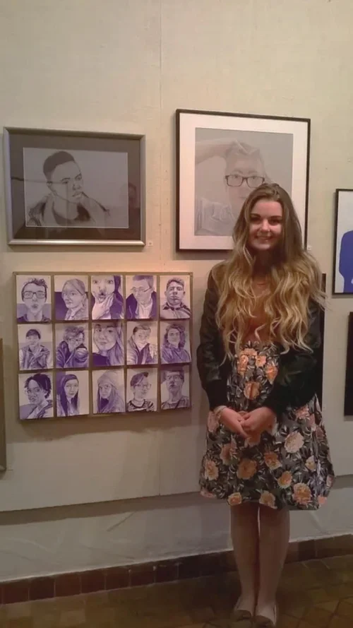 Elise Jackman as a young adult in front of a gallery of art, including several portraits she drew with a blue ballpoint pen